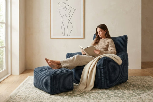 Lecture dans le fauteuil pouf Pola bleu nuit, pieds sur l'ottoman